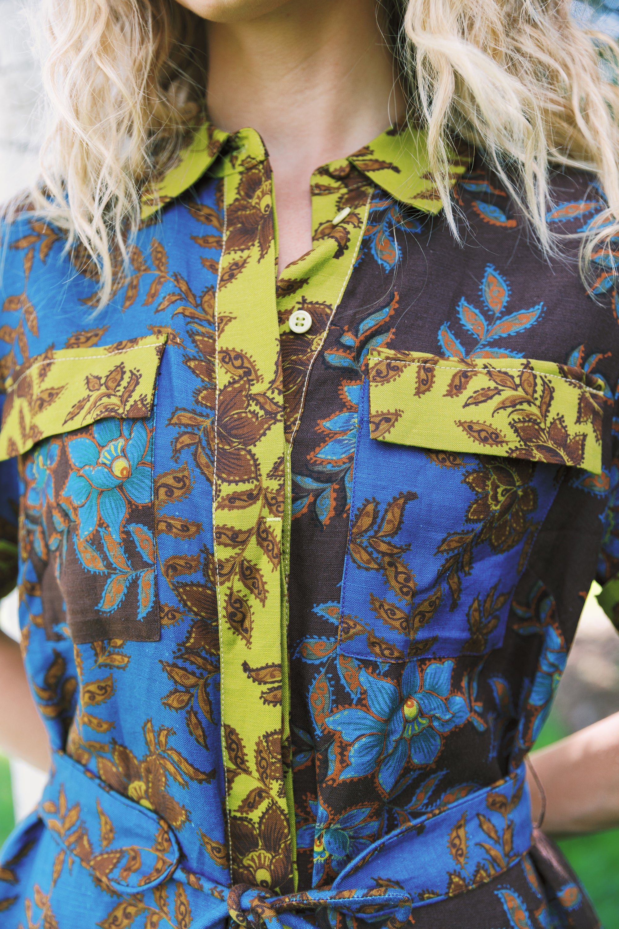Close-up of a person wearing a short-sleeve button-front shirt dress with a bold botanical print in blue, olive green, brown, and black.