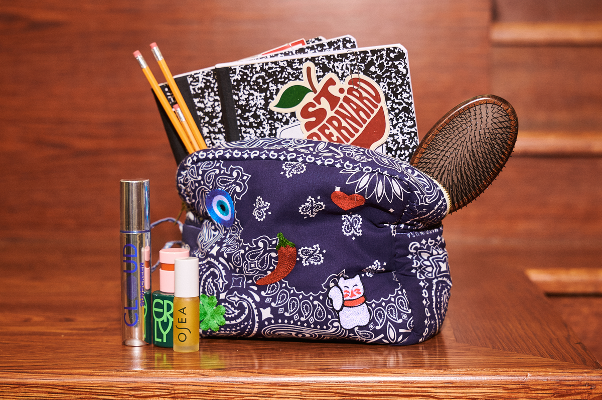 Navy bandana-print pouch filled with school notebooks, pencils, a hairbrush, and beauty essentials on a wooden tabletop.